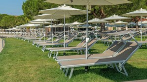 Rows of sun loungers with umbrellas, arranged on a grassy area with trees in the background. - Hotel Vile Park Premium (Piran)
