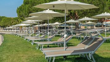De nombreuses chaises longues, protégées par des parasols, sont disposées sur une pelouse, avec des arbres en arrière-plan.