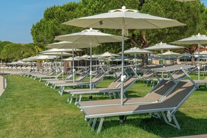 Rows of sun loungers with umbrellas, arranged on a grassy area with trees in the background. - Hotel Vile Park Premium (Piran)