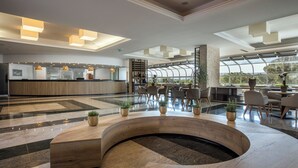 A modern lobby with a reception desk, seating area, and a large window offering a view of the outdoors. - Hotel Vile Park Premium (Piran)