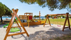 Un parque infantil con columpios y estructuras para escalar, cerca del agua y árboles.