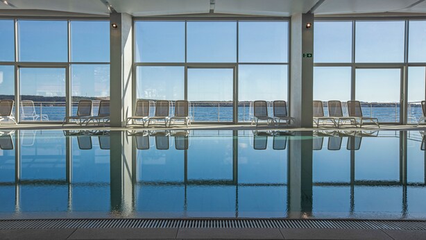 Piscina interior con vistas despejadas al exterior, rodeada de sillones de descanso.