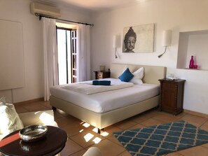 A hotel room with a bed, a nightstand, a wall-mounted lamp, a Buddha statue, and a window with curtains. - SON Manera Hotel Rural (MALLORCA)