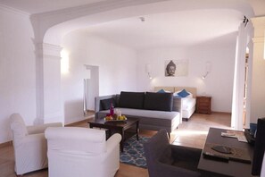 A living room with a grey sofa, white armchairs, a coffee table, and a bed with a headboard. - SON Manera Hotel Rural (MALLORCA)