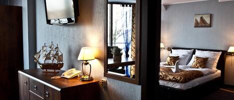 Una habitación de hotel con cama, cómoda, espejo, televisor y ventana con cortinas.