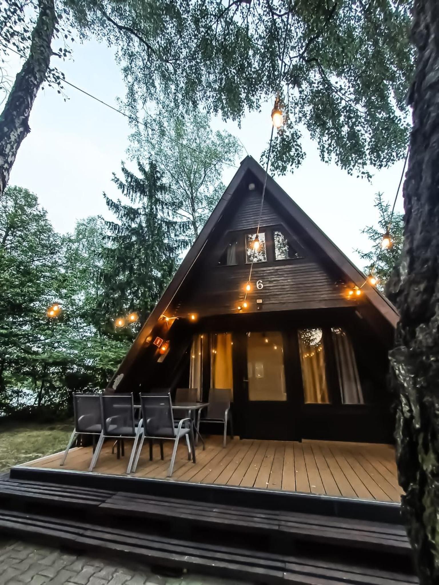 Una cabaña con terraza de madera, asientos exteriores y luces colgantes.