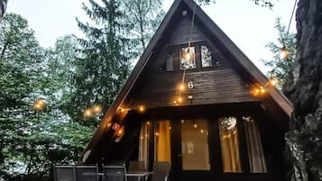A cabin with a wooden deck, outdoor seating, and string lights.