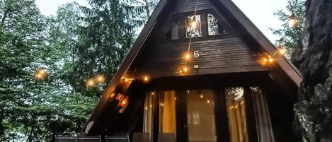 Una cabaña con terraza de madera, asientos exteriores y luces colgantes.