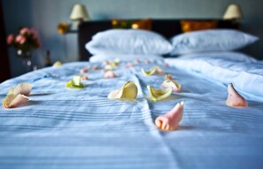 A bed with white linens and scattered rose petals.