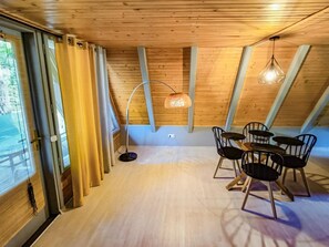 A room with a wooden ceiling, a dining table with chairs, and a hanging light fixture.