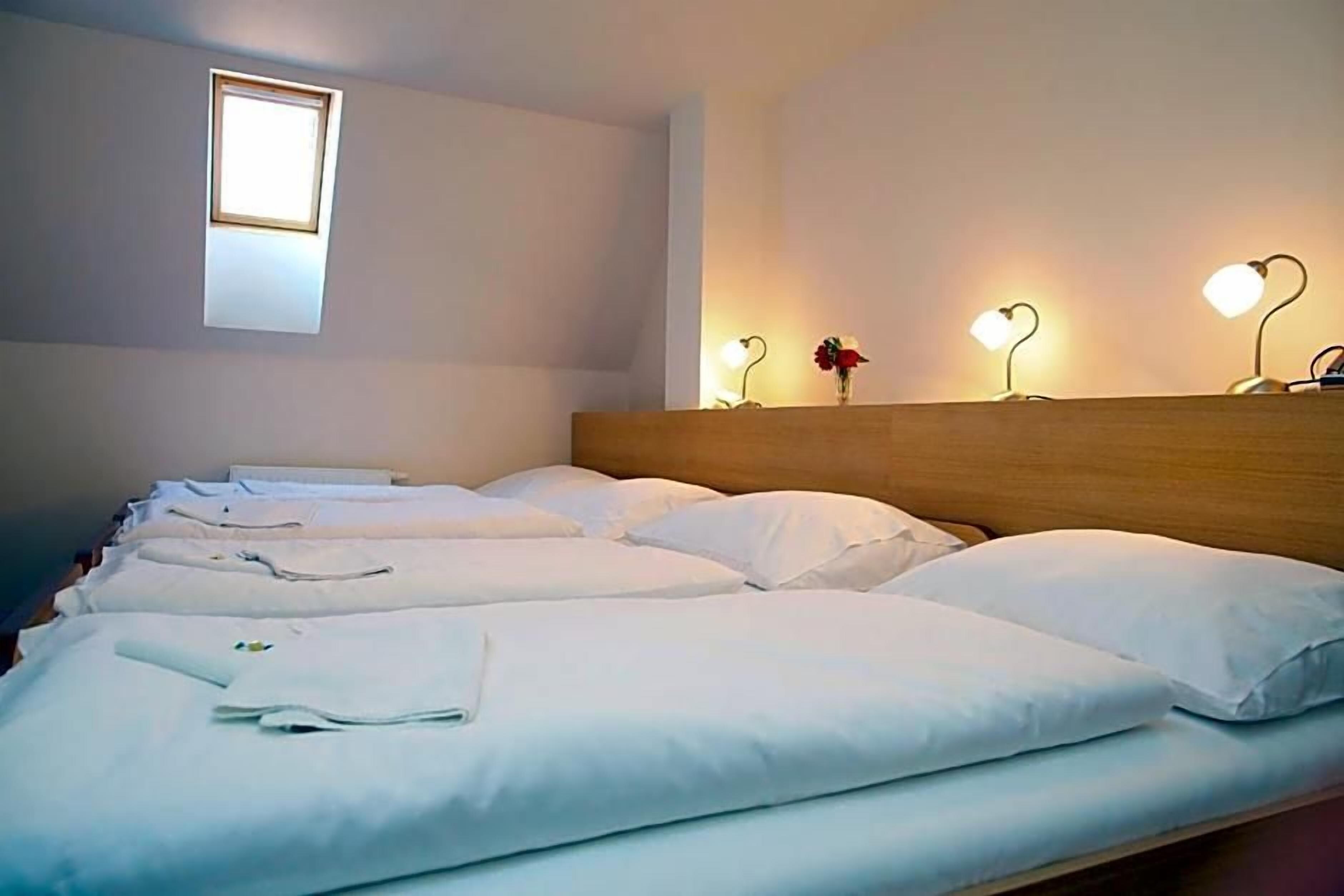 A hotel room with a neatly made bed, a wooden headboard, a small window, and three bedside lamps.