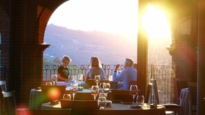 Un restaurante con terraza, vistas a las colinas y un atardecer.