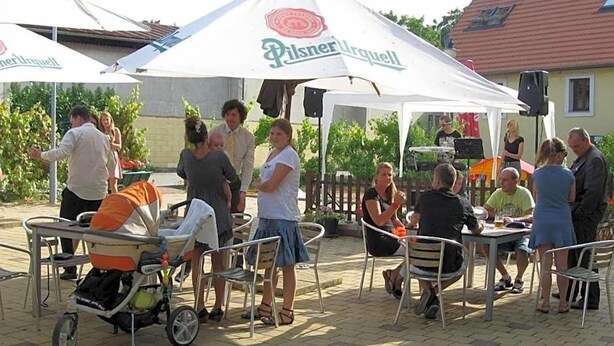 An outdoor seating area with tables and chairs, a baby stroller, and a tent with a logo. - Hotel Pod Sluncem (Třebíz)
