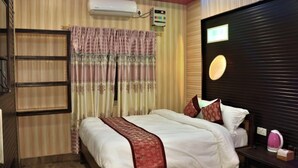 A hotel room with a bed, a bedside table, a lamp, a wall-mounted air conditioner, and a window with curtains. - Sauraha Boutique Resort (Sauraha)