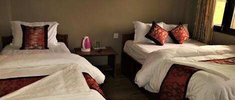 A hotel room with two beds, each with white bedding and red patterned pillows. There is a small table with a pink kettle and a vase.