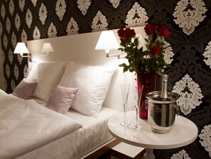 Quarto de hotel com cama bem arrumada, um vaso de rosas vermelhas e um minibar.