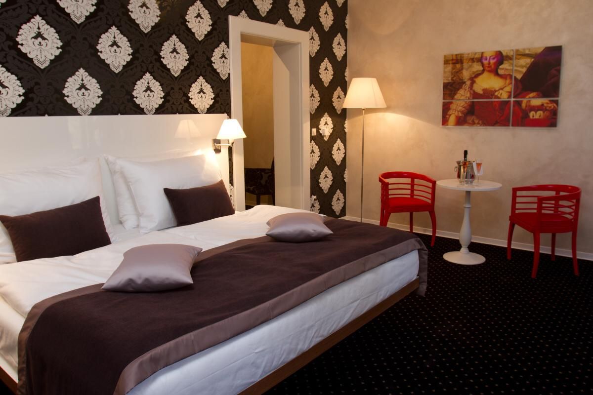 Habitación de hotel con una cama grande, dos lámparas de noche, una mesita con una silla y un cuadro en la pared.