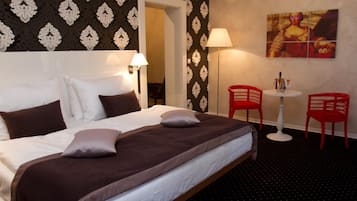 Habitación de hotel con una cama grande, dos lámparas de noche, una mesita con una silla y un cuadro en la pared.