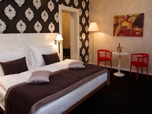 Ein Hotelzimmer mit einem großen Bett, zwei roten Sessel, einem kleinen Tisch und einem Bild an der Wand.