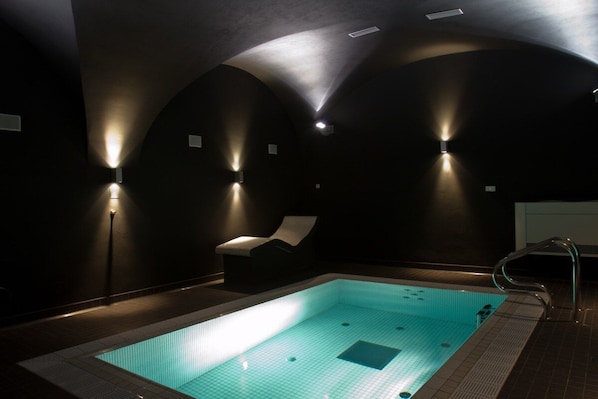 A dimly lit indoor swimming pool with a single lounge chair and a metal pool ladder. - EA Hotel Tereziánský Dvůr (Hradec Kralove)
