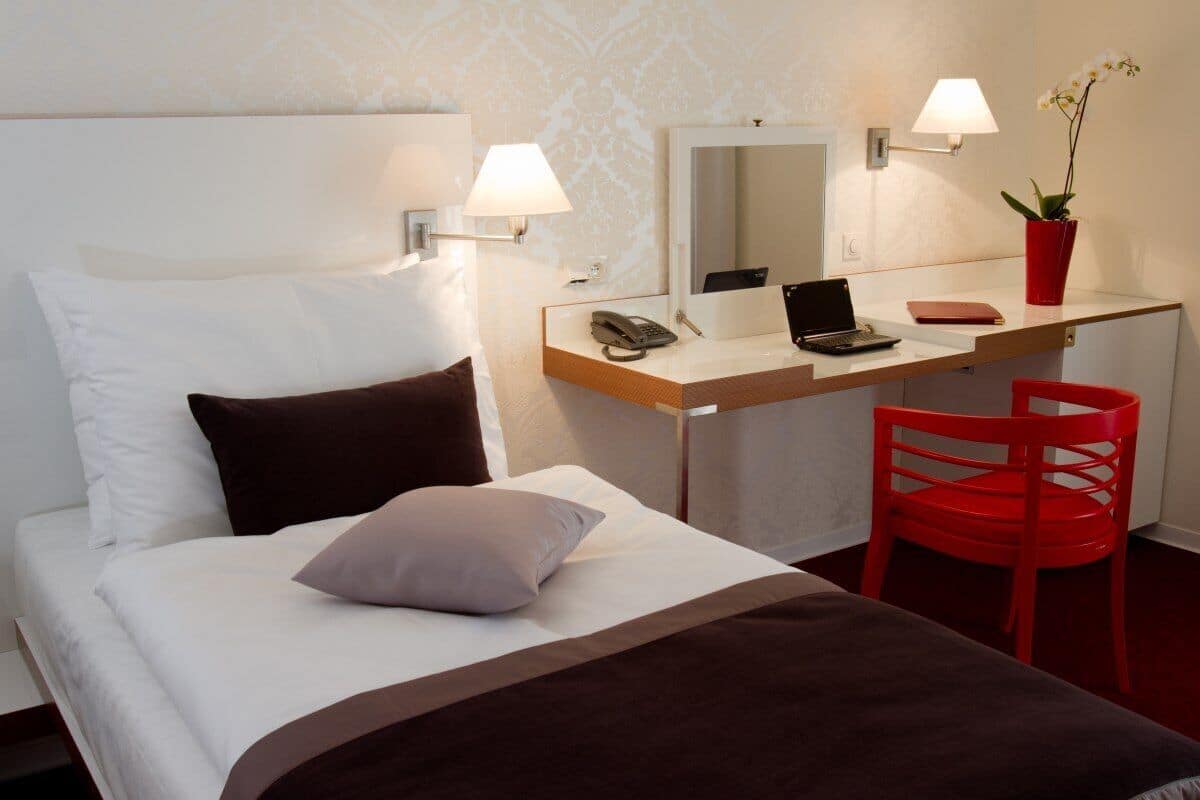 Habitación de hotel con una cama, un escritorio con una computadora portátil, un teléfono y una silla roja.