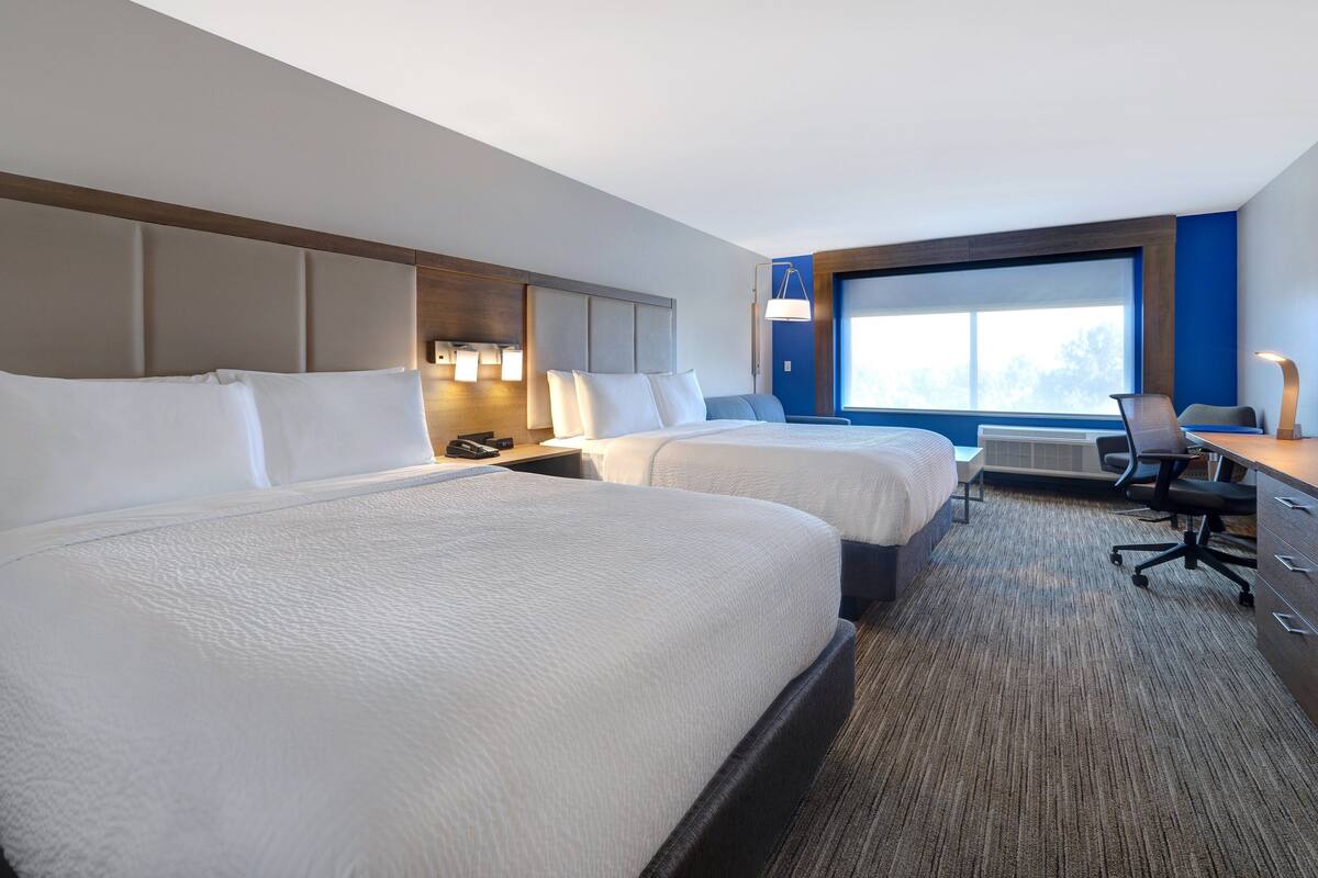 A hotel room with two beds, a desk, a chair, and a large window.
