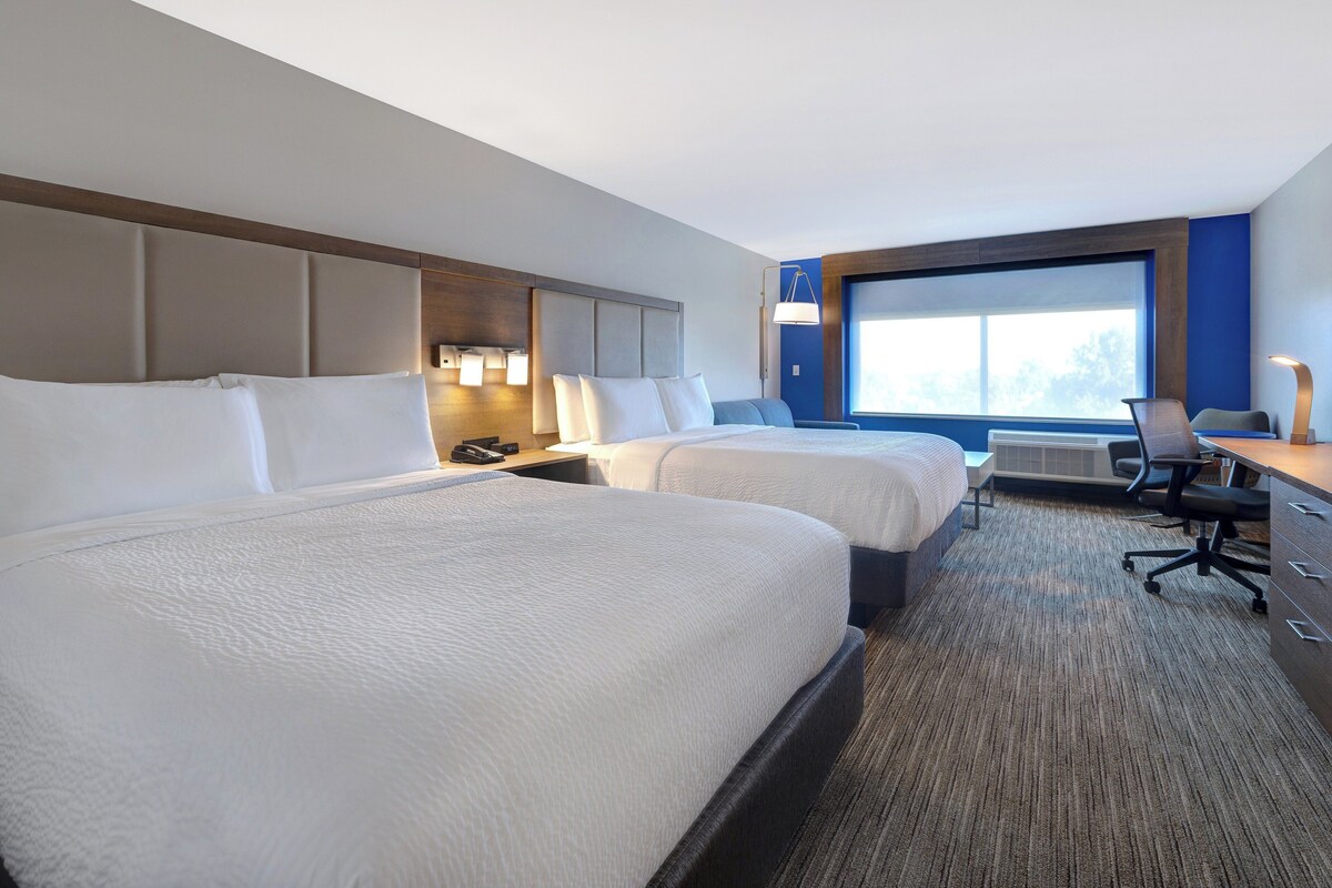Een hotelkamer met twee bedden, een bureau, een stoel en een groot raam.