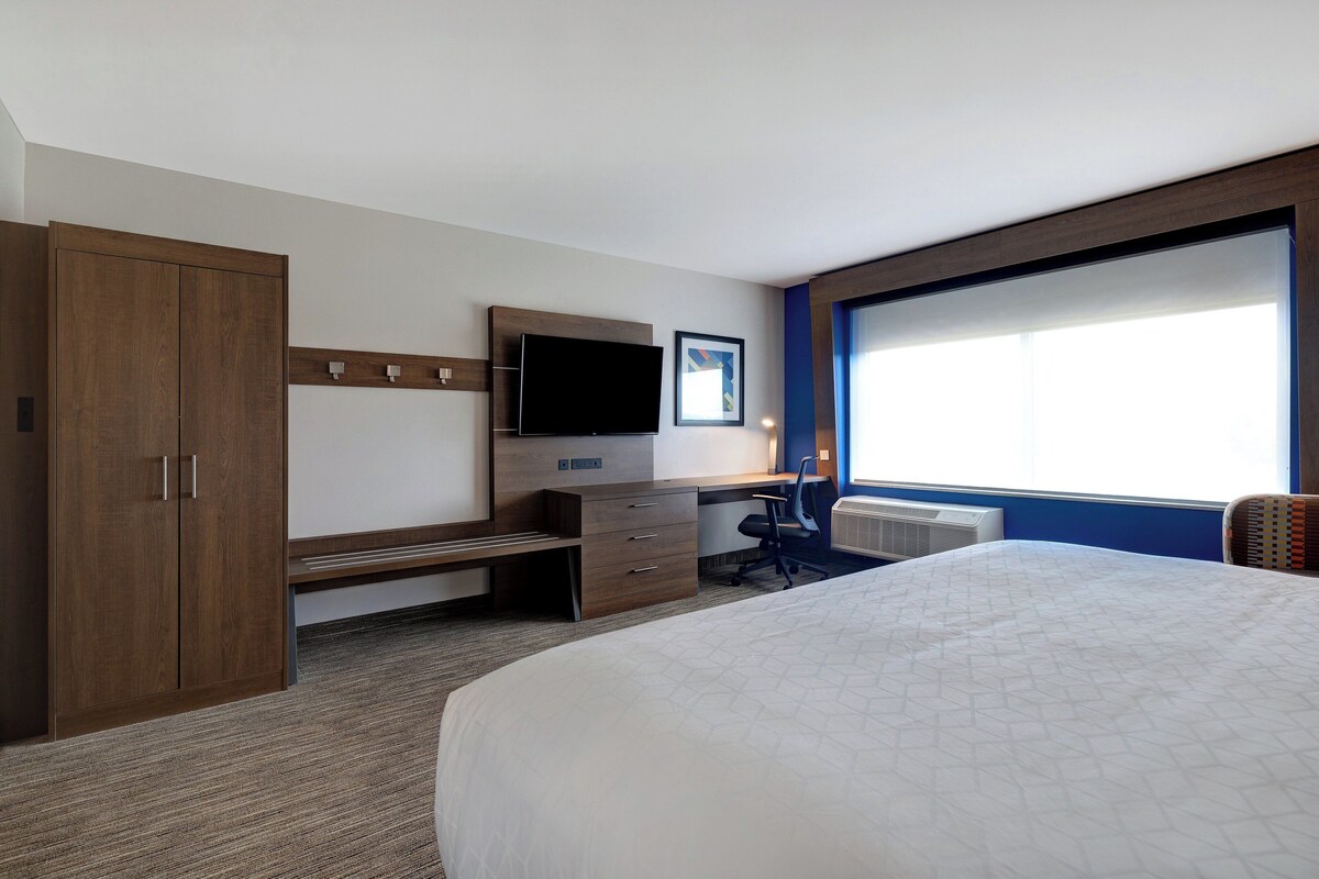 Een hotelkamer met een groot bed, een bureau met stoel, een televisie en een kledingkast.