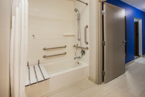A modern bathroom with a walk-in shower, grab bars, and a door leading to another room.