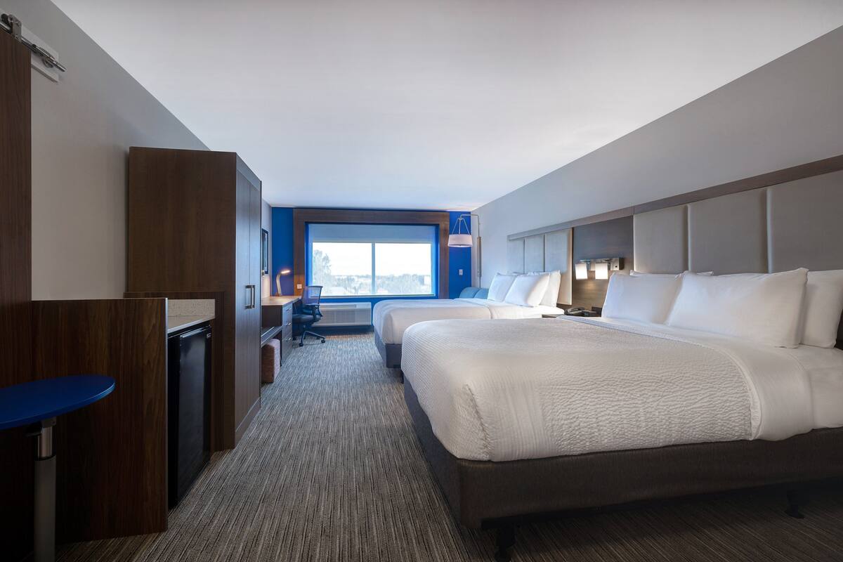 A hotel room with a large bed, a desk, a chair, and a view of the city through the window.
