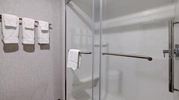 Une salle de bain avec une douche à parois de verre, des murs recouverts de carreaux blancs et un porte-serviettes avec trois serviettes.
