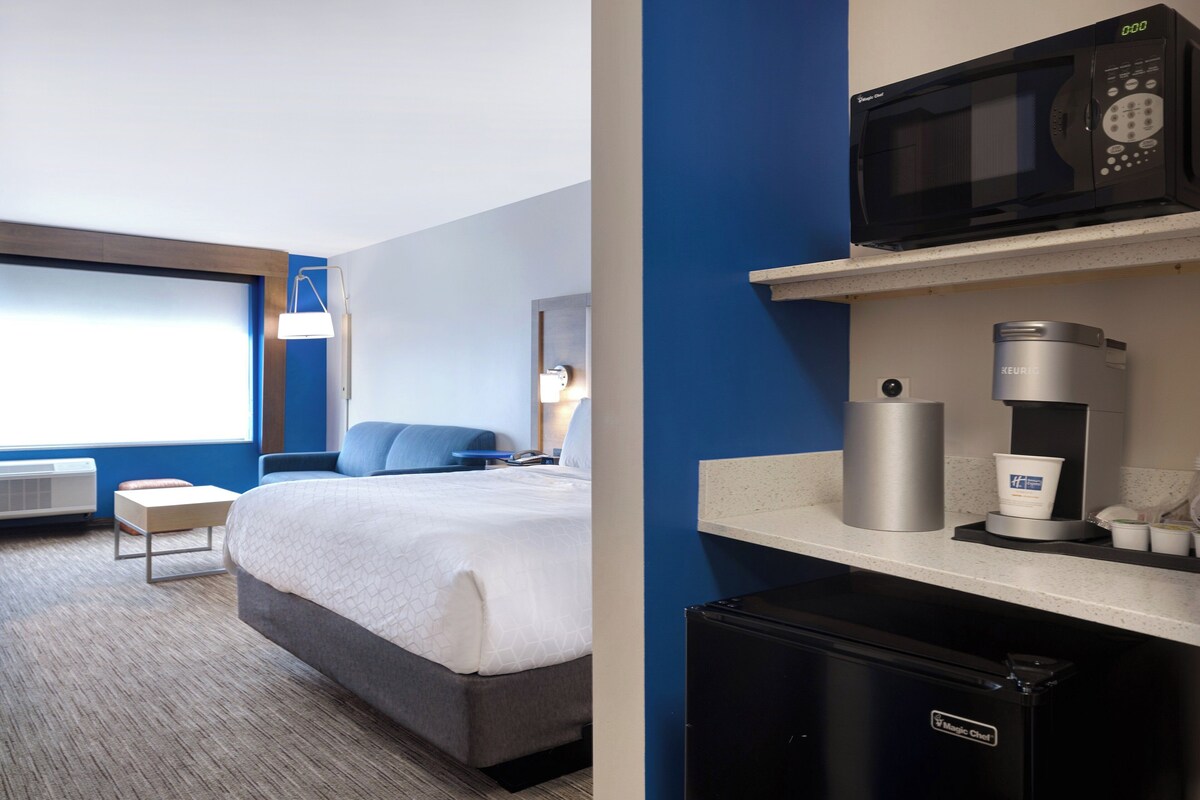 Een hotelkamer met een bed, een bureau, een magnetron, een koffiezetapparaat en een koelkast.