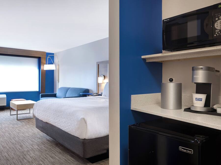 Een hotelkamer met een bed, een bureau, een magnetron, een koffiezetapparaat en een koelkast.