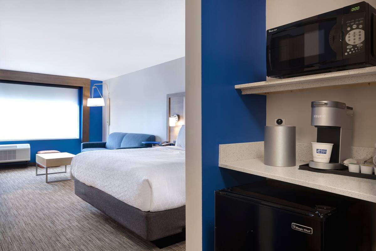A hotel room with a bed, a desk, a microwave, a coffee maker, and a refrigerator.