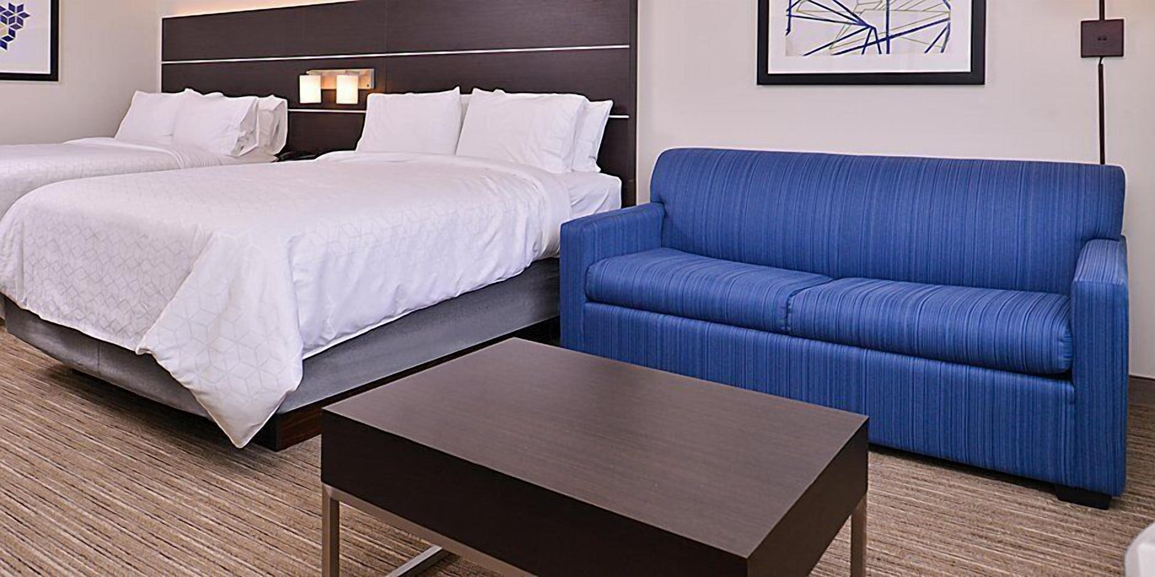 Una habitación de hotel con dos camas, un sofá azul y una pequeña mesa.