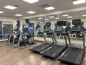 Ett gym med löpband, crosstrainers och motionscyklar, utrustat med digitala skärmar och en stor spegelvägg.