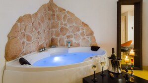 A spa room with a stone wall, a bathtub, a wine glass, and candles.