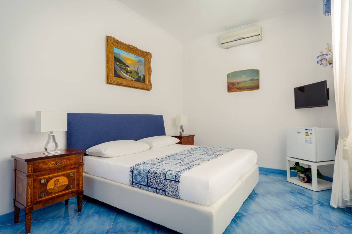 Een slaapkamer met een bed, nachtkastje, televisie en een wandairconditioner.
