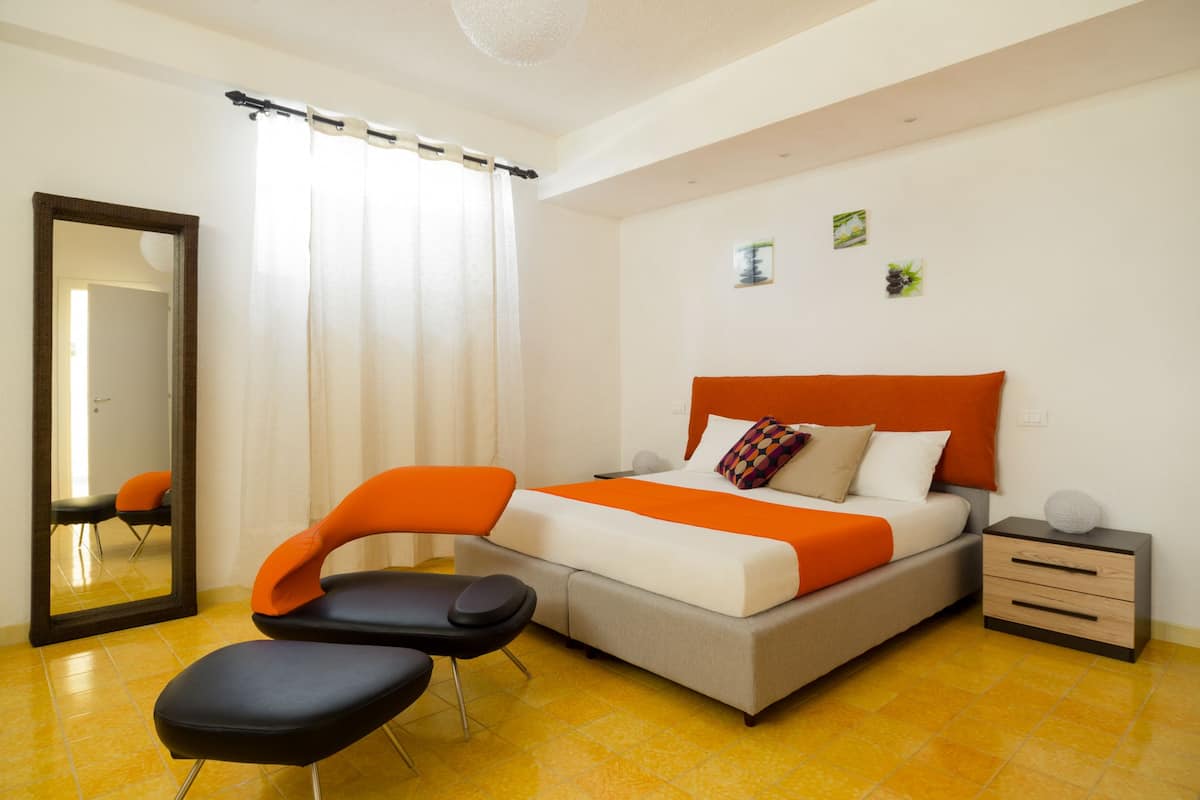 Een moderne slaapkamer met een bed, een stoel, een nachtkastje en een spiegel.