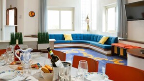 A dining area with a curved blue sofa, a TV mounted on the wall, and a dining table set with plates, glasses, and a bottle of wine.