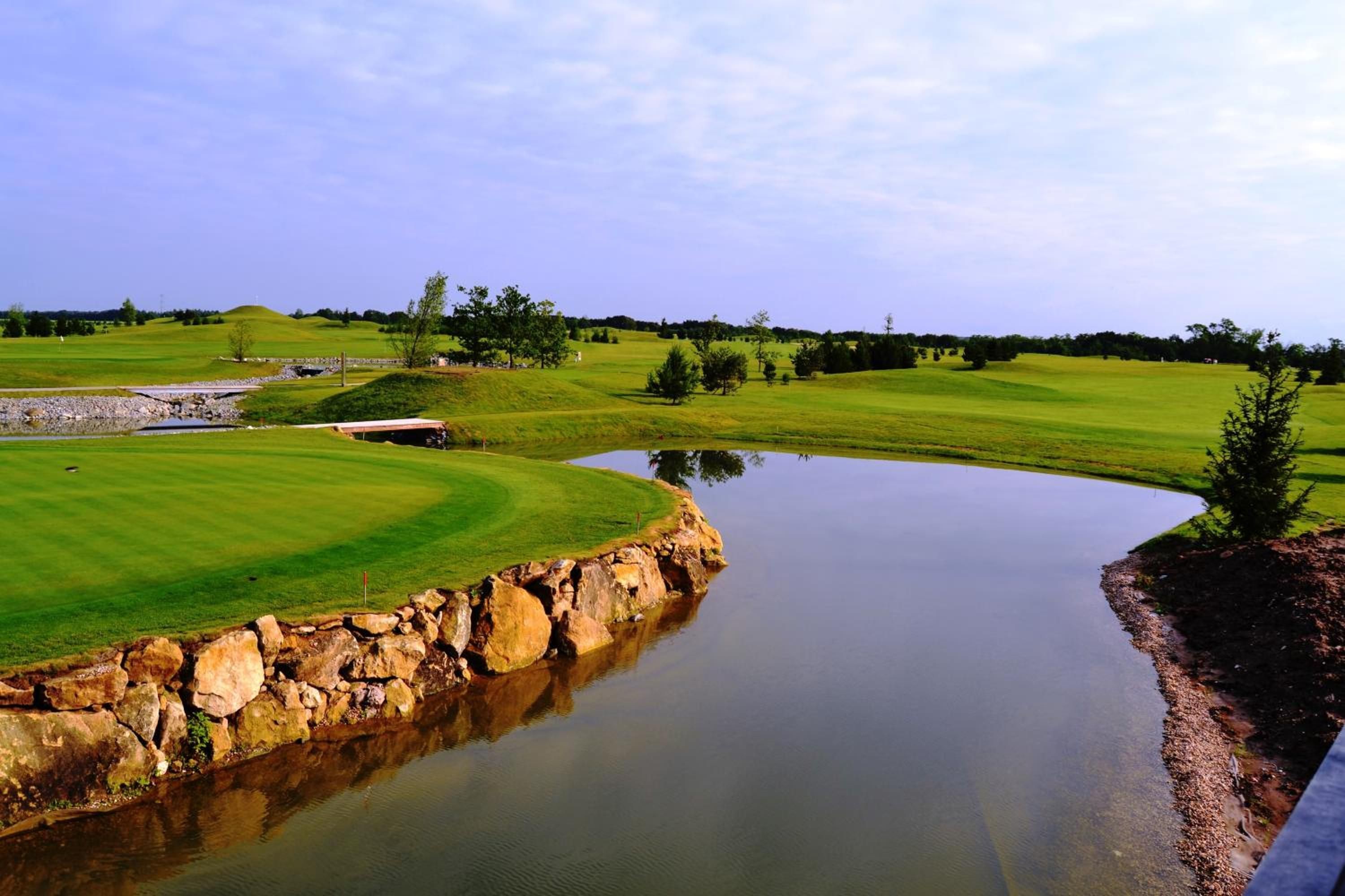 Un campo de golf con un estanque, muros de piedra y cielo despejado.