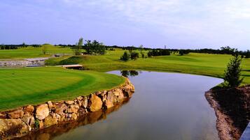 Camp de golf amb un estany, murs de pedra i un cel clar.