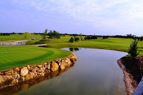 A golf course with a pond, stone walls, and a clear sky.