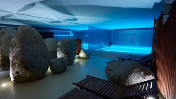 Un área de piscina interior con rocas grandes, bancos de madera y una vista despejada de la piscina.