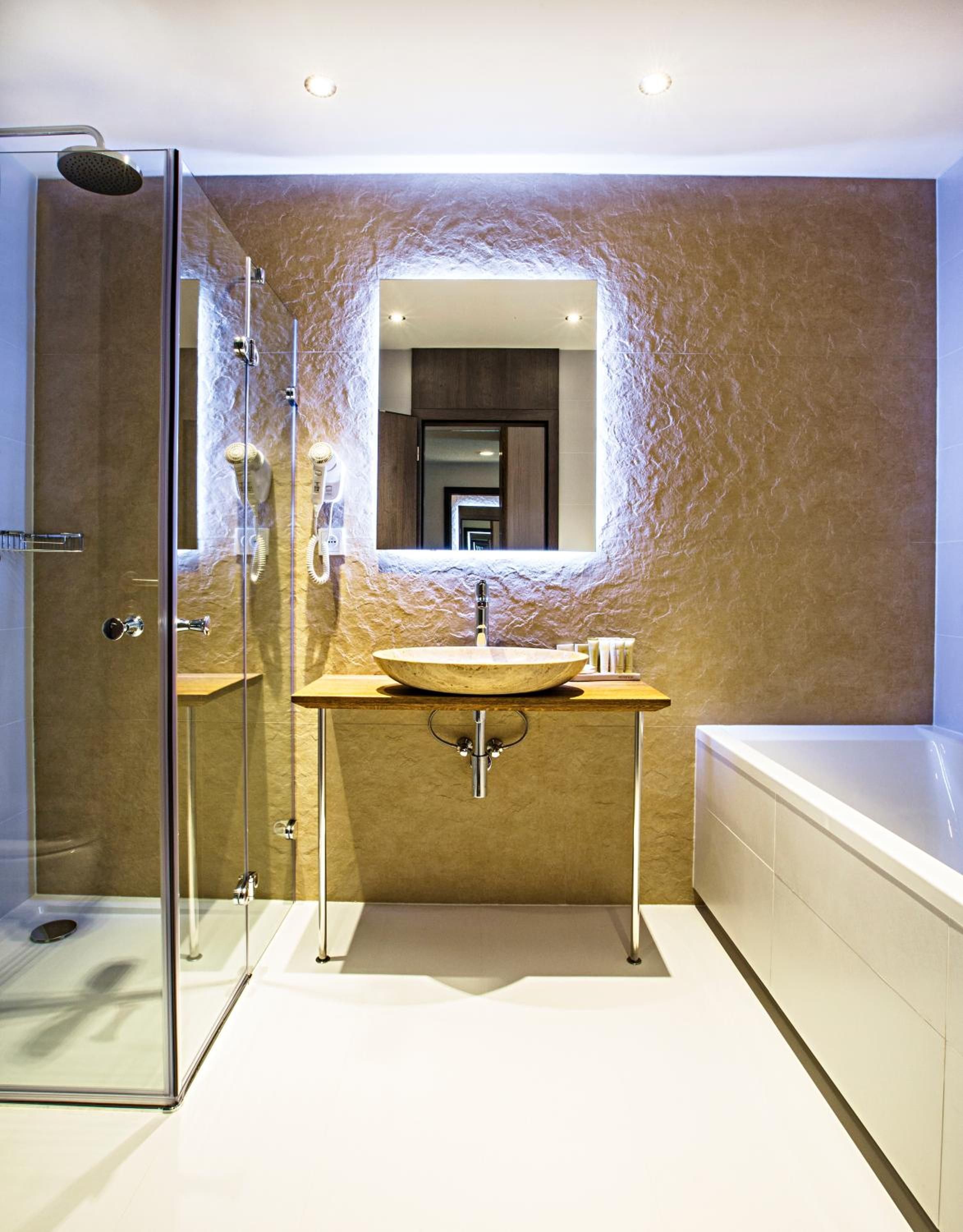 A modern bathroom with a glass-enclosed shower, a large mirror, a wooden vanity, and a separate bathtub.