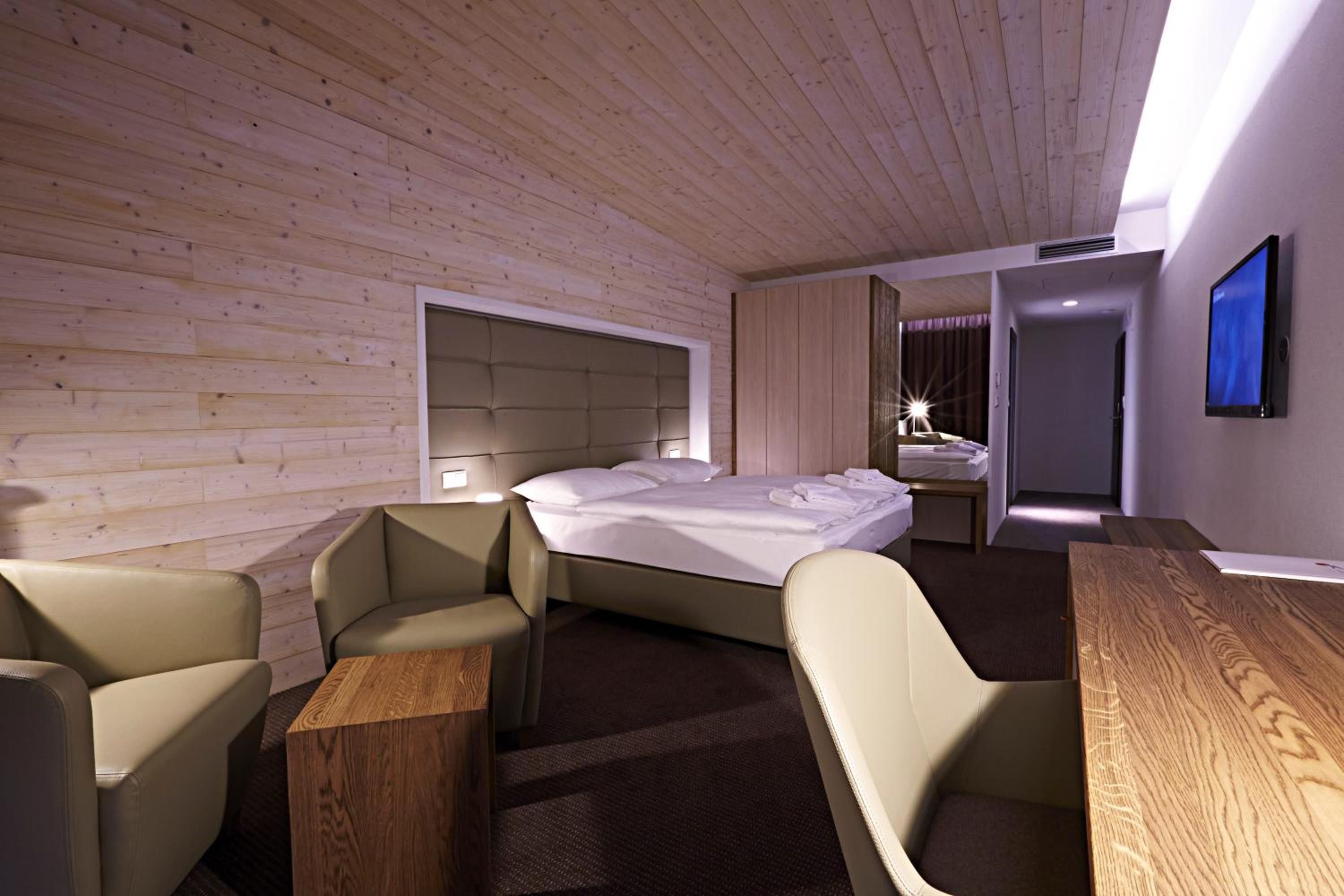 Ein modernes Hotelzimmer mit Holzbalkendecke, einem Bett, einem Schreibtisch und einem Stuhl.