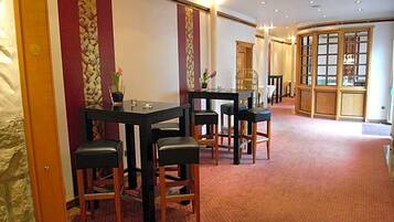 A hotel room with a dining area featuring a table and chairs, a large window with a view, and a carpeted floor.