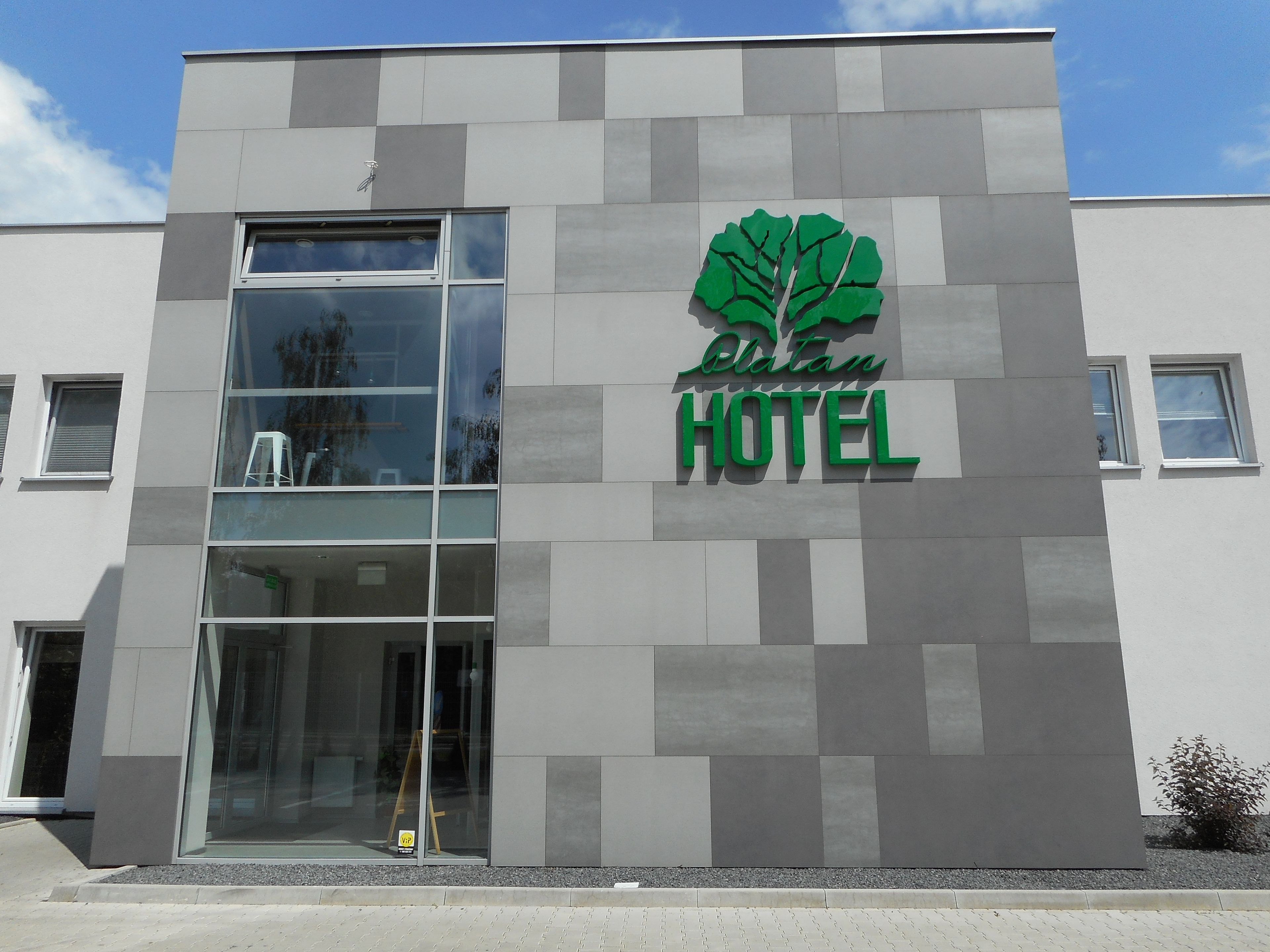 Un moderno edificio de hotel con una amplia entrada de vidrio y un logotipo que muestra un árbol estilizado.