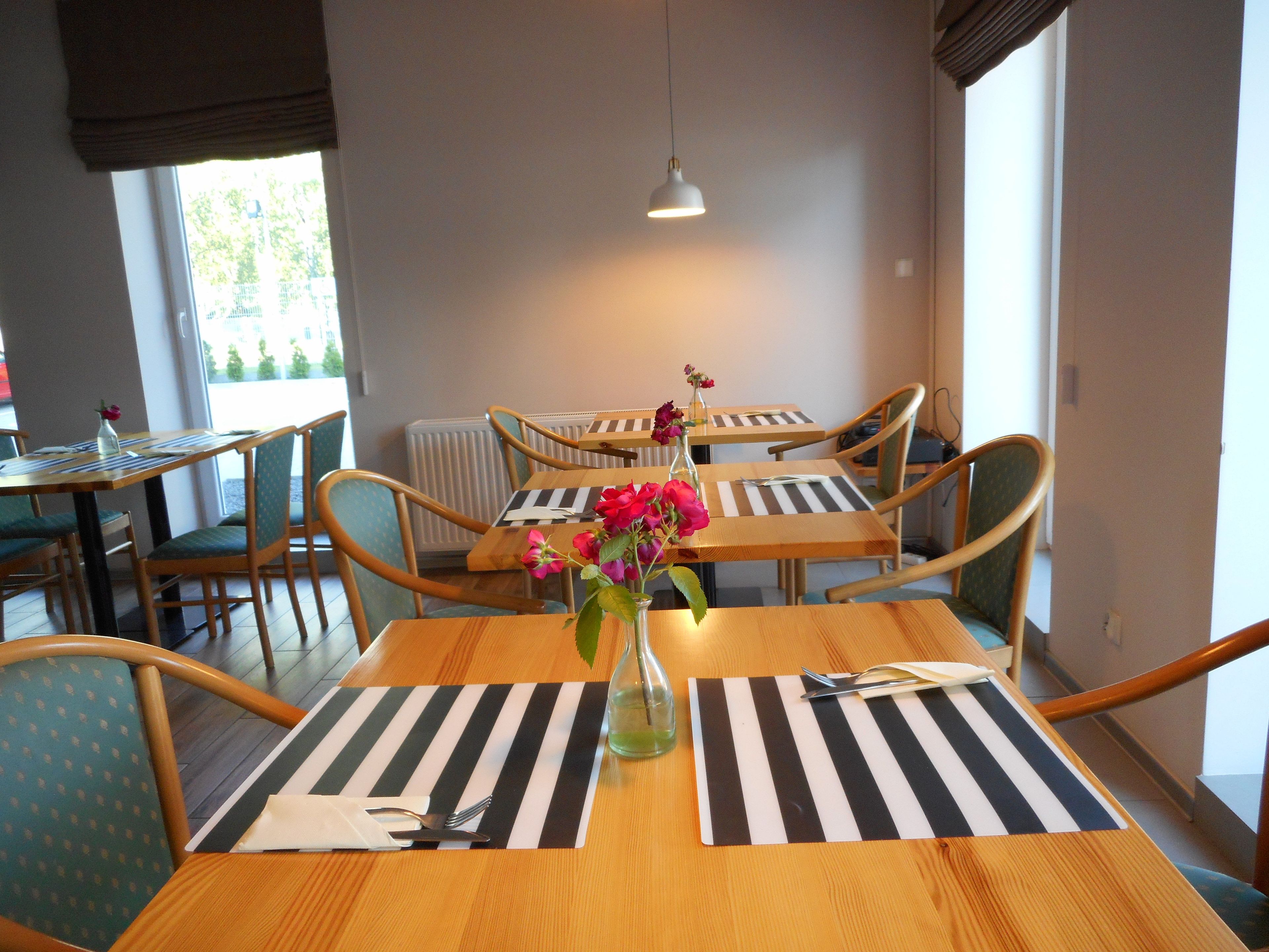 Comedor con mesas y sillas de madera, individuales a rayas negras y blancas, y un jarrón con flores rosadas.