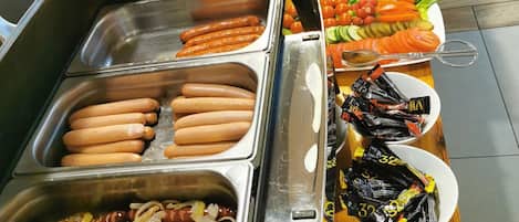 A buffet with various food options including hot dogs, salads, and bread.